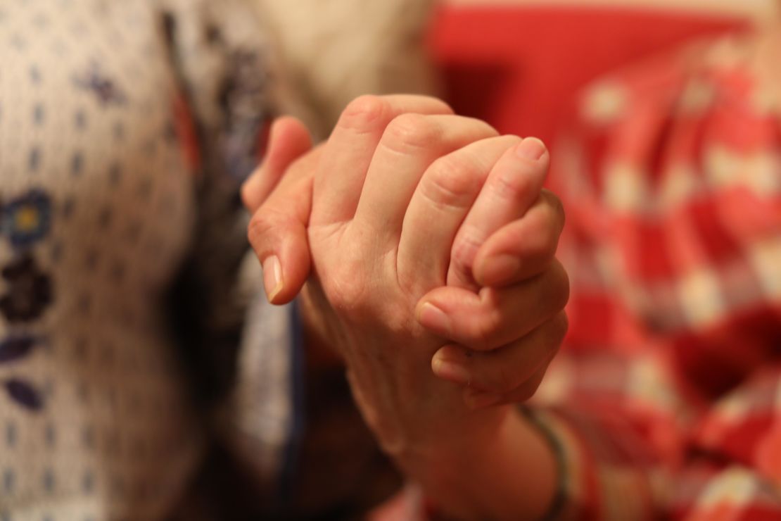 The two mothers clasp hands in the apartment.
