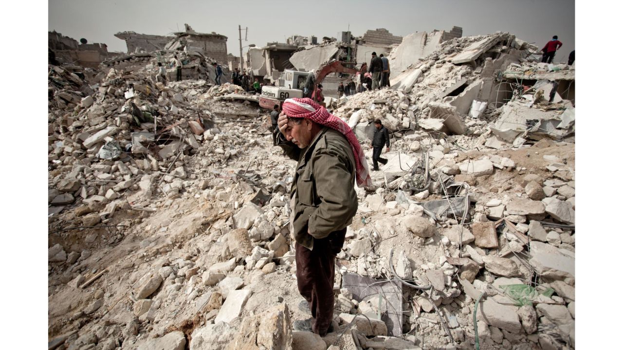 A Syrian man reacts while standing on the rubble of his house while others look for survivors and bodies in Aleppo. 