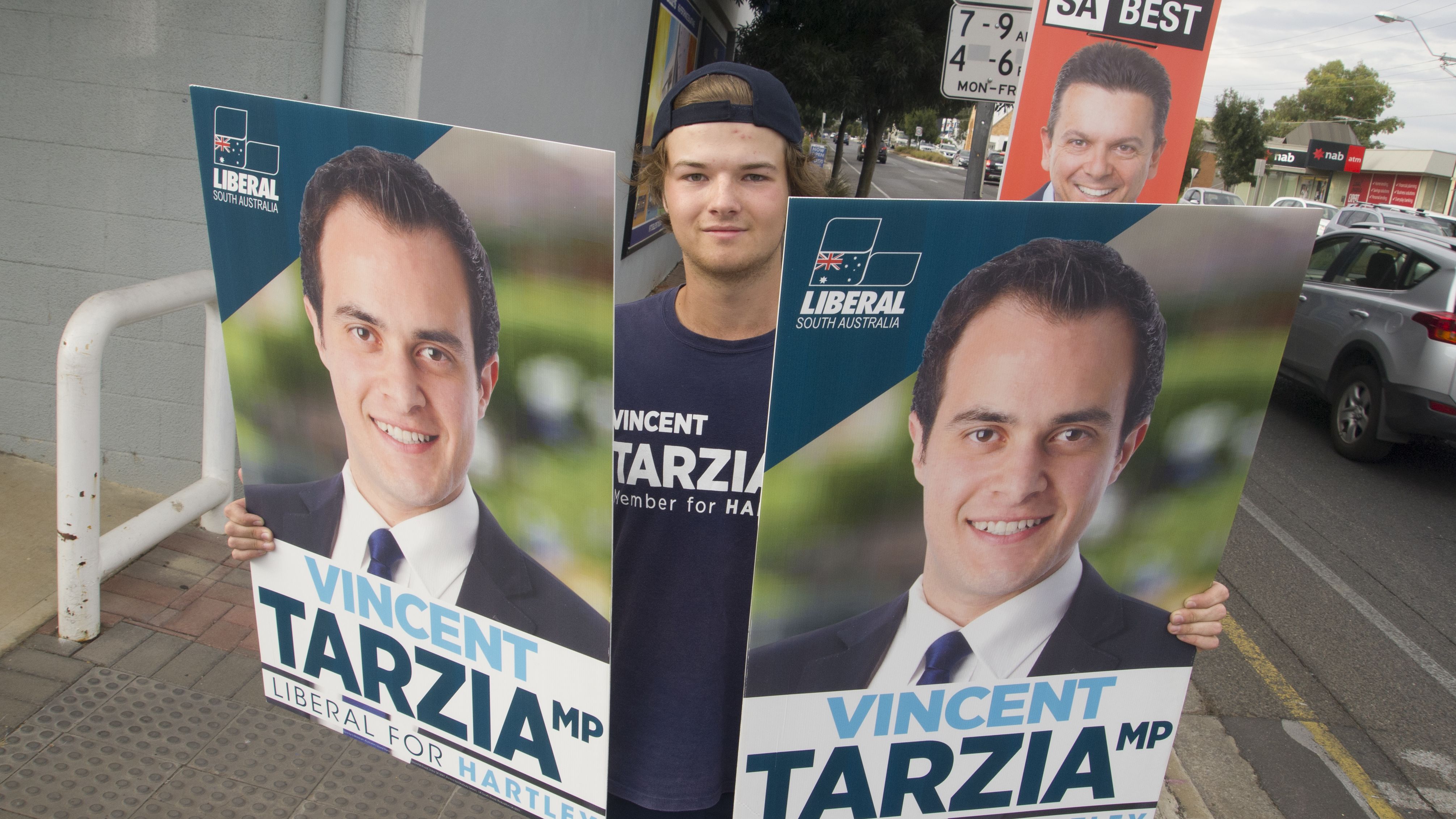 A campaign volunteer holds signs for the Liberal candidate for Hartley, who's running against Nick Xenophon from SA Best.