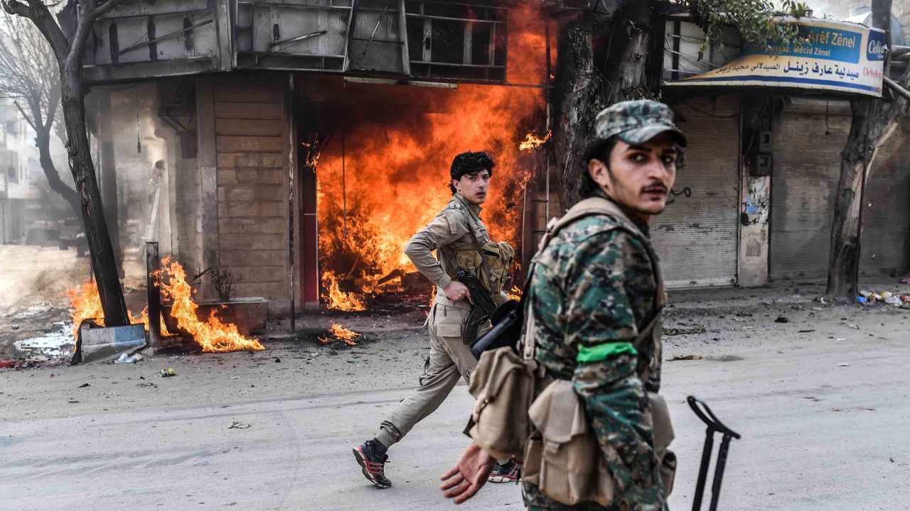 Rebel fighters walk past a burning shop in Afrin.