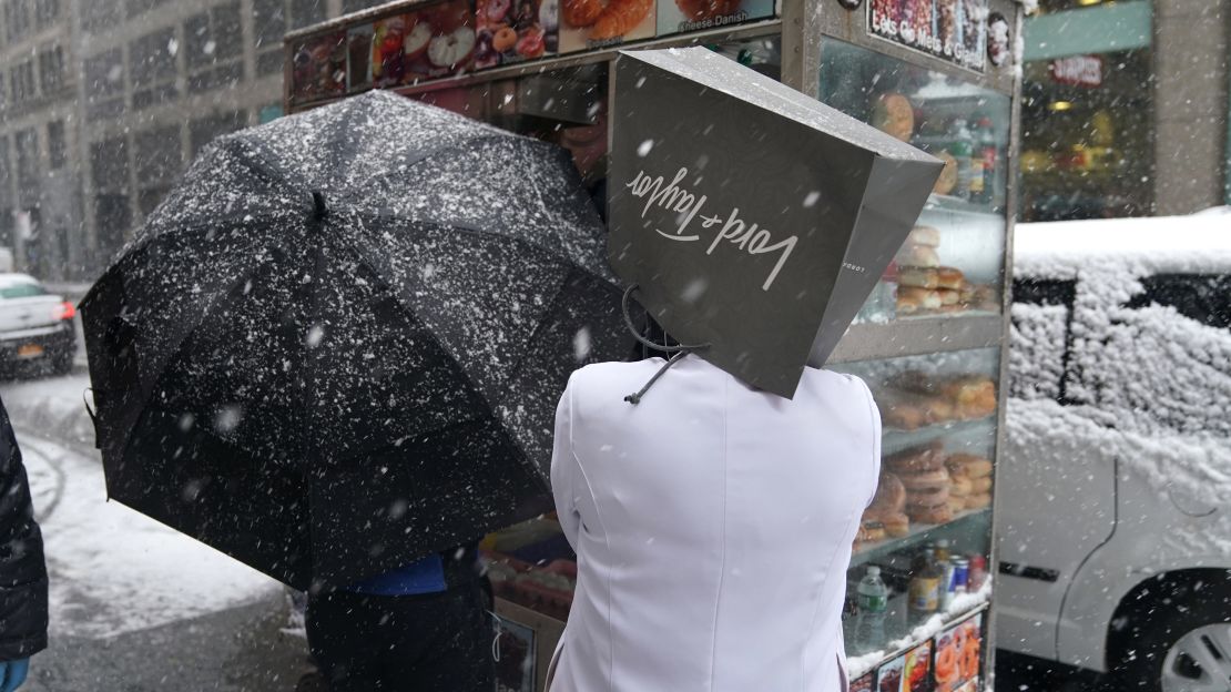 A Lord & Taylor employee takes cover from snow Wednesday on Fifth Avenue in New York. 