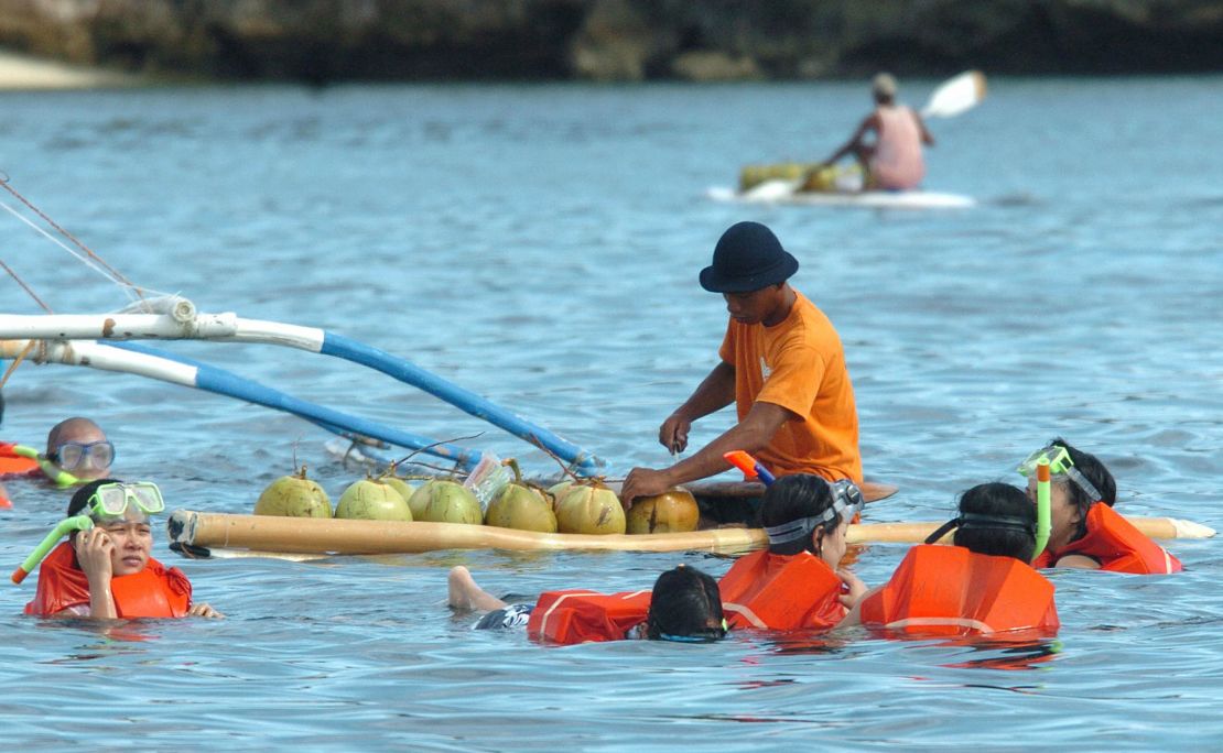 A man on a surfboard sells fresh coconut juice to people swimming in the waters off the central Philippine resort island in this shot dated 2005.