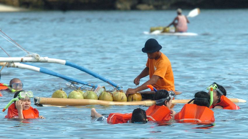 BORACAY, PHILIPPINES: TO GO WITH STORY "PHILIPPINES-TOURISM-ENVIRONMENT-BORACAY" A man on a surfboard sells fresh coconut juice to people swimming in the waters off the central Philippine resort island of Boracay, 11 June 2005. Despite the image of the island of pristine beaches and crystal-clear waters that attracts thousands of tourists, Boracay faces a worsening garbage problem, just one of several dilemmas that the island must contend with as more and more people flock to its beaches. AFP PHOTO/Joel NITO (Photo credit should read JOEL NITO/AFP/Getty Images)