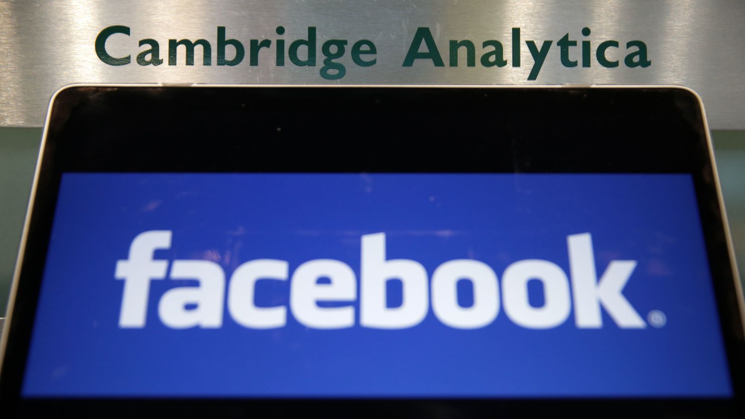 A laptop showing the Facebook logo is held alongside a Cambridge Analytica sign at the entrance to the building housing the offices of Cambridge Analytica, in central London on March 21, 2018.  