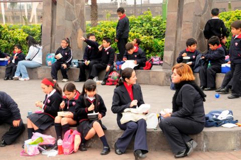 Middle school students enjoy lunch outdoors in Lima, Peru. Many children pack lunches brought from home that include juice boxes, fruit and traditional dishes.