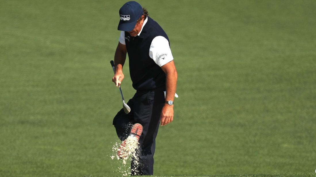 Three-time Masters champion Phil Mickelson cleans his shoes after a bunker shot on Friday.