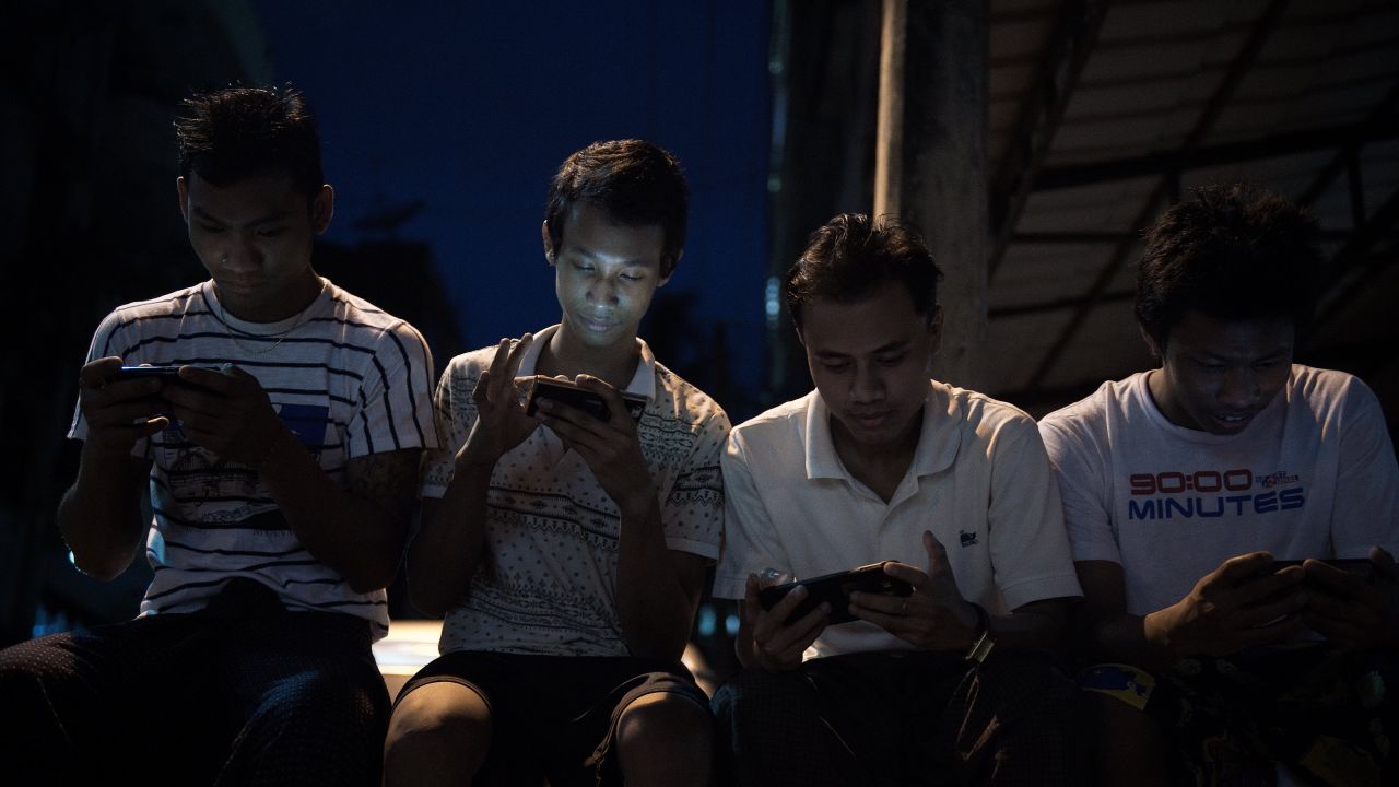 Young men browse Facebook on their smartphones as they sit in a street in Yangon.
