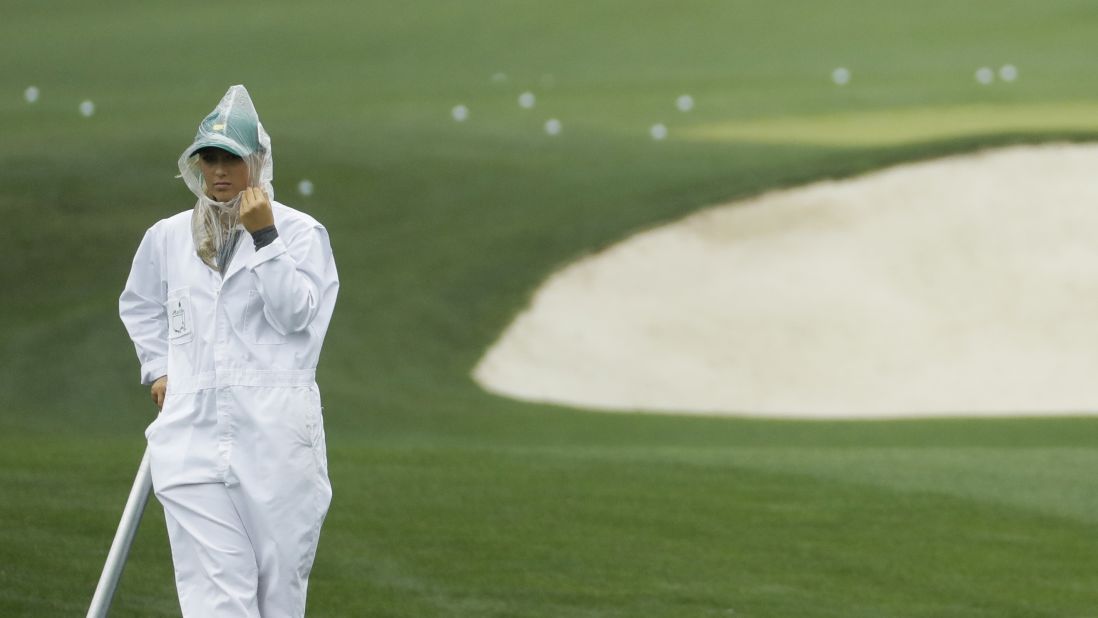 A course worker covers her head during some rain at the practice range during the third round at the Masters golf tournament Saturday. 