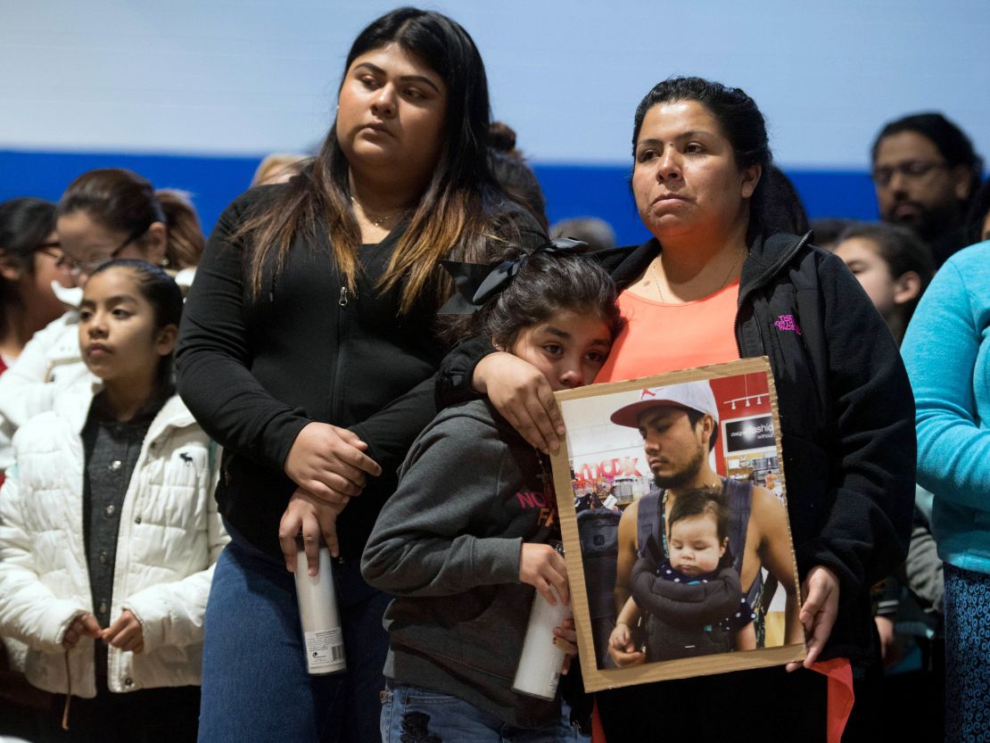 At a prayer vigil, Esmeralda Baustista holds a photo of her brother Luis Bautista-Martinez, detained in the ICE raid. With her is daughter Yemaya and friend Yaqueline Cruz. 