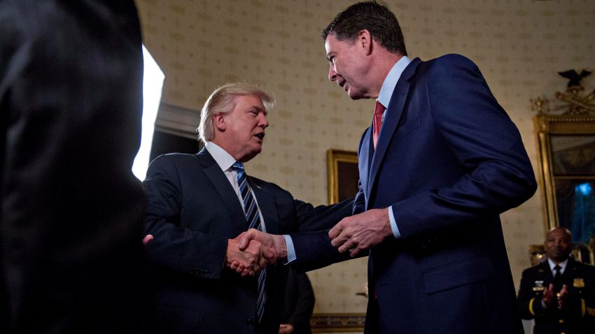 WASHINGTON, DC - JANUARY 22: U.S. President Donald Trump (C) shakes hands with James Comey, director of the Federal Bureau of Investigation (FBI), during an Inaugural Law Enforcement Officers and First Responders Reception in the Blue Room of the White House on January 22, 2017 in Washington, DC. Trump today mocked protesters who gathered for large demonstrations across the U.S. and the world on Saturday to signal discontent with his leadership, but later offered a more conciliatory tone, saying he recognized such marches as a "hallmark of our democracy." (Photo by Andrew Harrer/Pool/Getty Images)