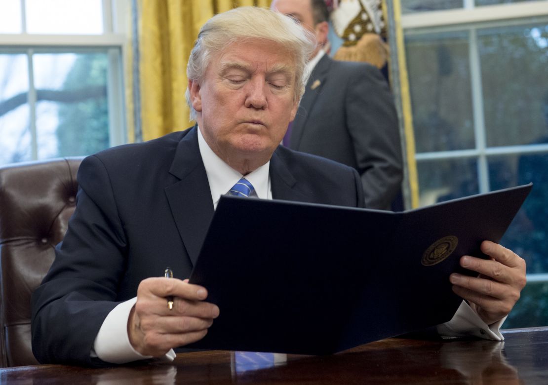 President Donald Trump reading the executive order withdrawing the US from the Trans-Pacific Partnership prior to signing it in the Oval Office on January 23, 2017.