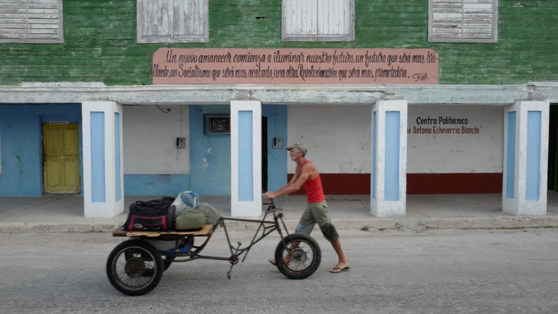 A Cuban man wheels his possessions in Gibara, Cuba, under a sign quoting Fidel Castro:  "A new dawn shall begin to illuminate our future, a future that shall be more brilliant, a Socialism that shall be more refined, a Revolutionary work that will be more promising."