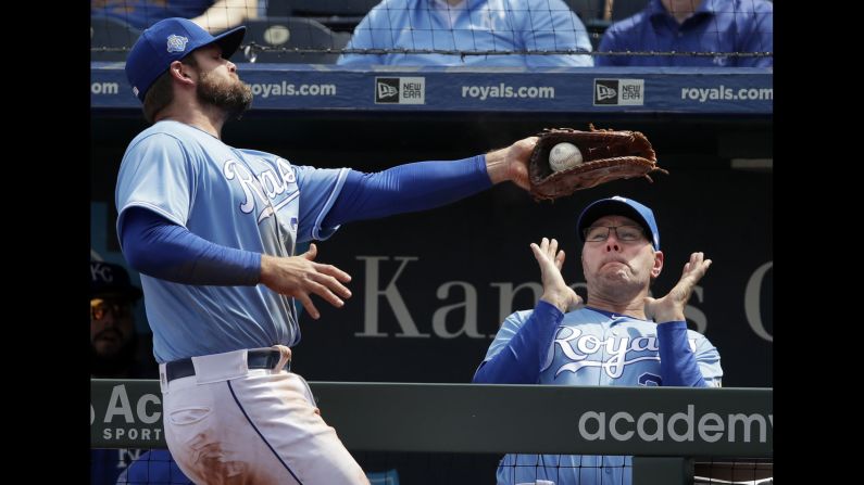 Kansas City Royals first baseman Lucas Duda, left, catches a foul ball where Kansas City Royals pitching coach Cal Eldred stands in the dugout during a baseball game against the Seattle Mariners on Wednesday, April 11, in Kansas City, Missouri. 