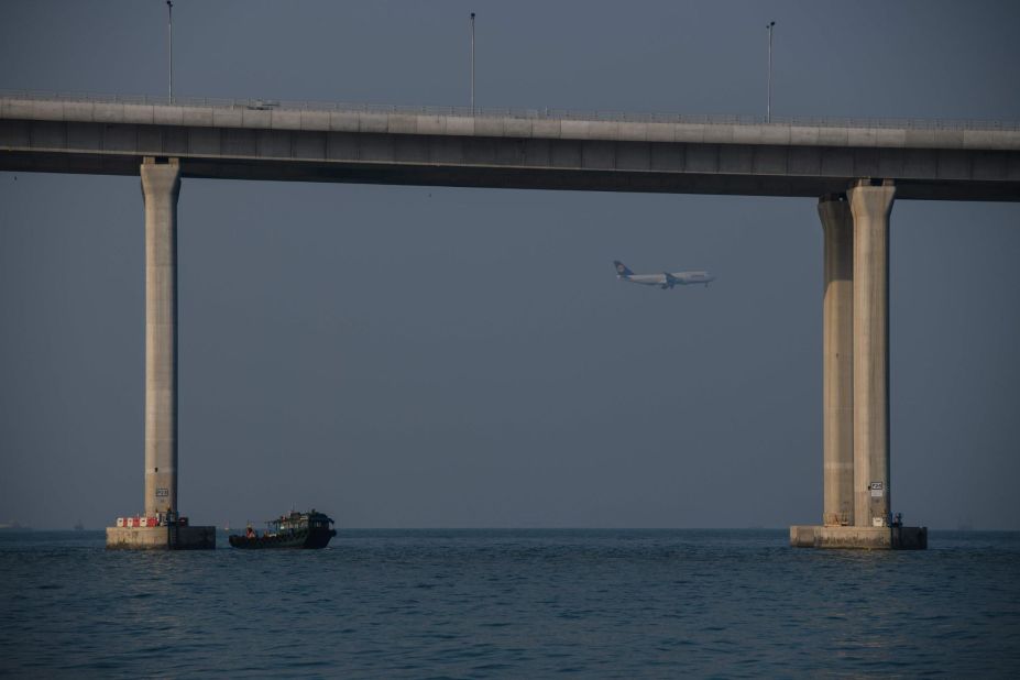 A boat transporting construction workers' berths next to a column of the Hong Kong-Zhuhai-Macau Bridge as a plane prepares to land at Hong Kong's international airport. 