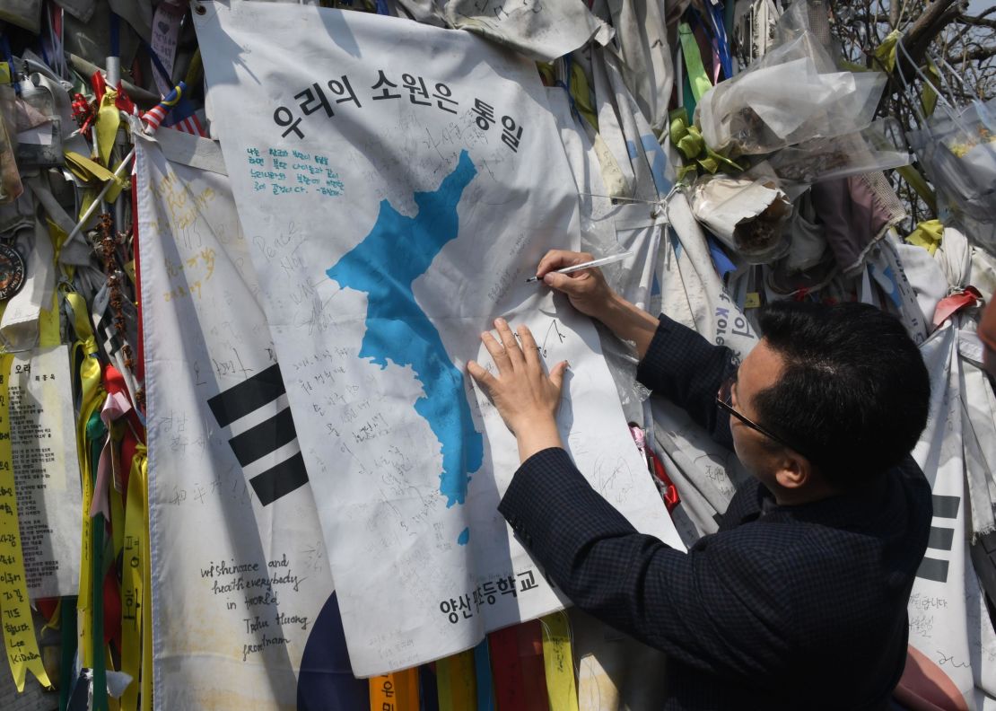 A man writes an inscription calling for peace and reunification on a "Unification flag" hanging at a military fence at Imjingak peace park in Paju near the demilitarized zone dividing the two Koreas on April 26, 2018.
