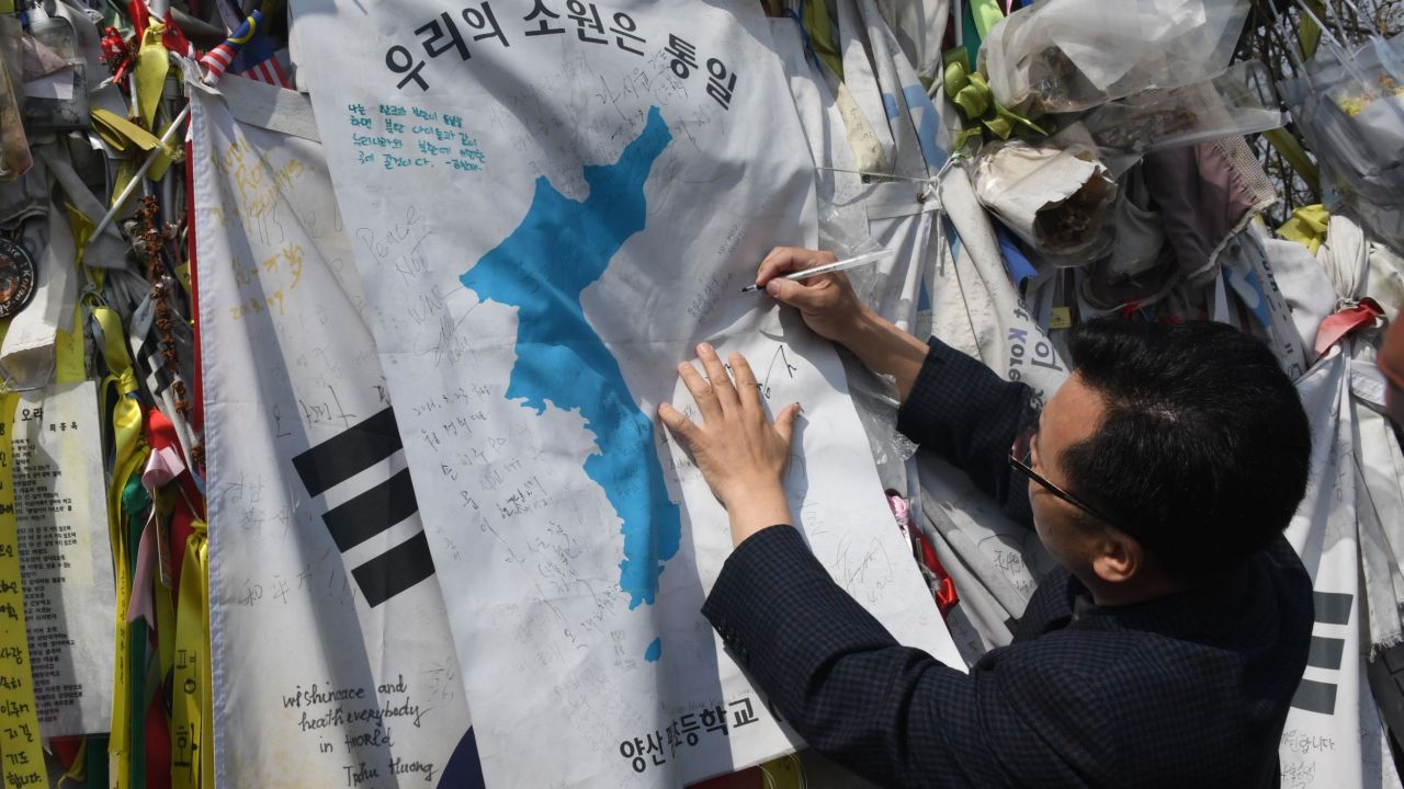 A man writes an inscription calling for peace and reunification on a "Unification flag" hanging at a military fence at Imjingak peace park in Paju near the demilitarized zone dividing the two Koreas on April 26, 2018.