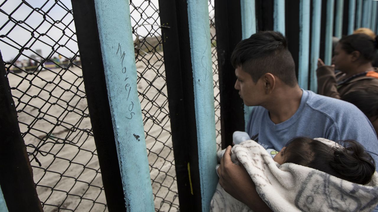 A member of the Central American migrant caravan, holding a child, looks through the border wall toward a group of people gathered on the U.S. side, as he stands on the beach where the border wall ends in the ocean, in Tijuana, Mexico, Sunday, April 29, 2018. U.S. immigration lawyers are telling Central Americans in a caravan of asylum-seekers that traveled through Mexico to the border with San Diego that they face possible separation from their children and detention for many months. They say they want to prepare them for the worst possible outcome. (AP Photo/Hans-Maximo Musielik)