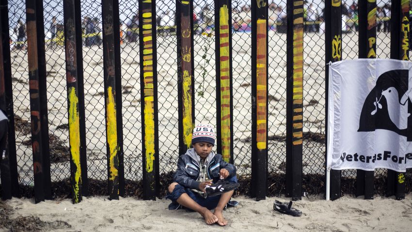 A Central American migrant boy travelling in the "Migrant Via Crucis" caravan removes sand of his shoes during a demonstration at the US/Mexico Border at Tijuana's beaches, Baja California state, Mexico, on April 29, 2018. - The US has threatened to arrest around 100 Central American migrants if they try to sneak in from the US-Mexico border where they have gathered, prompting President Donald Trump to order troop reinforcements on the frontier. (Photo by GUILLERMO ARIAS / AFP) (Photo credit should read GUILLERMO ARIAS/AFP/Getty Images)