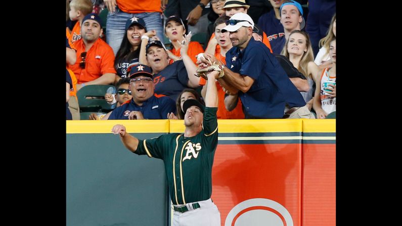 Oakland's Stephen Piscotty leaps to catch a ball, but a fan in Houston beat him to it on Sunday, April 29. Umpires reviewed <a href="index.php?page=&url=https%3A%2F%2Ftwitter.com%2FMLBReplays%2Fstatus%2F990678807827894272" target="_blank" target="_blank">the play</a> and ruled that the hitter was out because of fan interference.