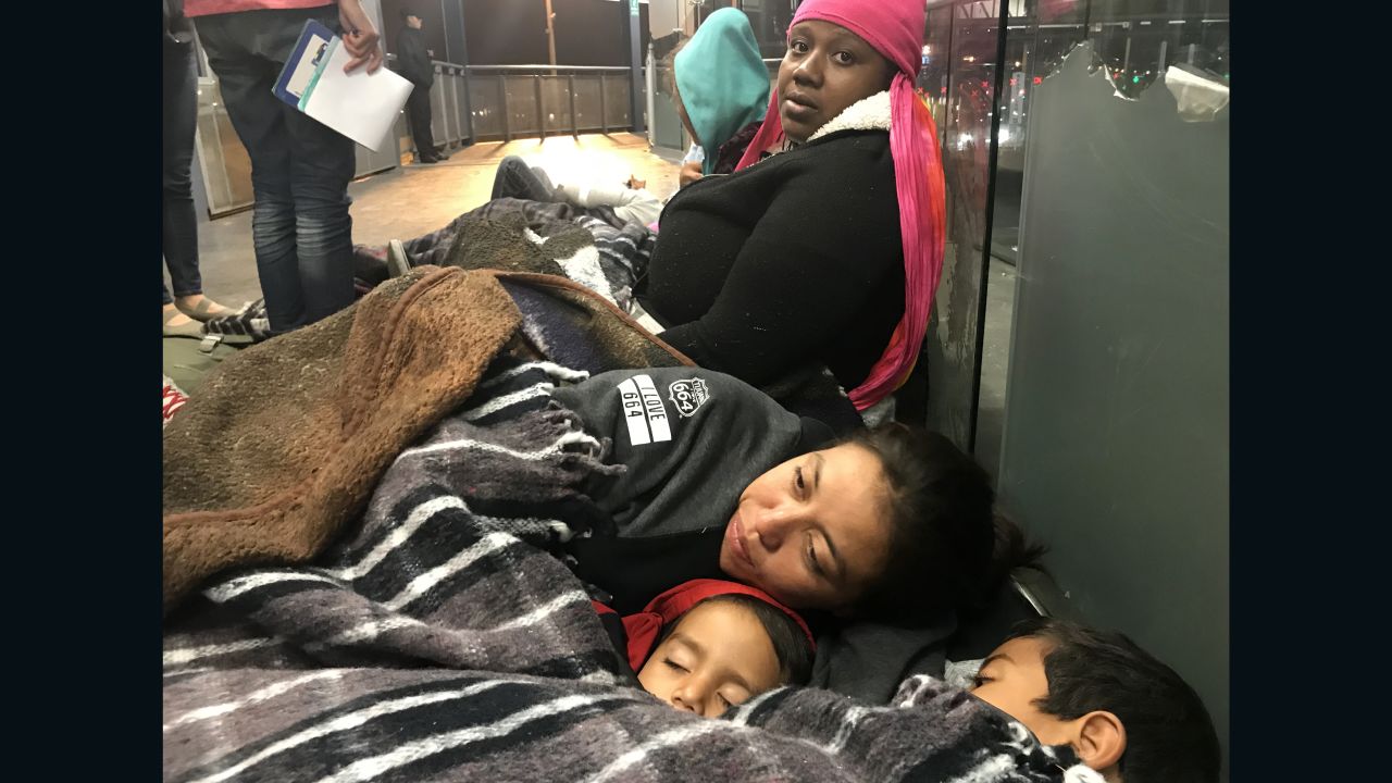 Migrants Tesla Rich (sitting) and Gabriela Hernandez with sons Jonathan and Omar, wait together to be allowed into the border post.