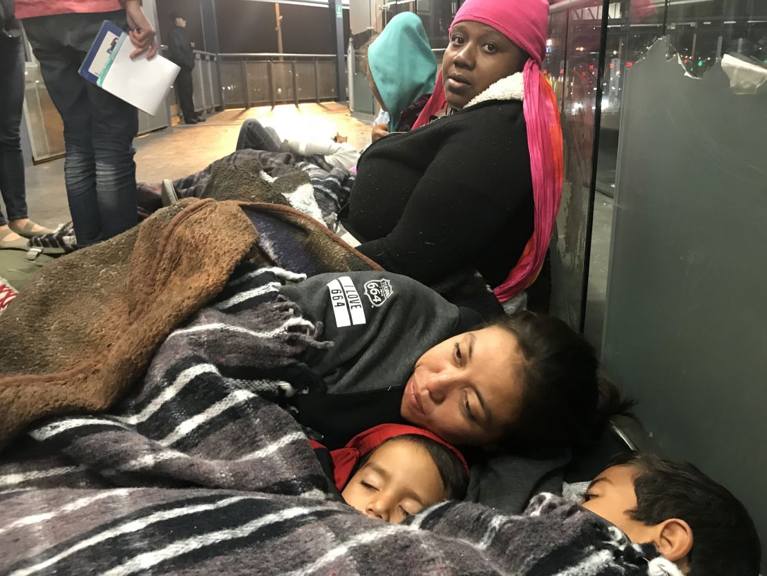 Migrants Tesla Rich, sitting, and Gabriela Hernandez, with sons Jonathan and Omar, try to keep warm as they await border officials to call them for asylum processing. 