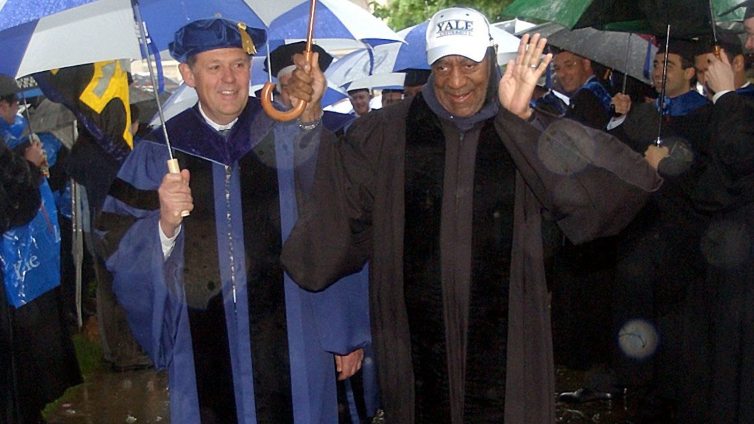 Bill Cosby, center right, waves to graduates as he walks in a rain-soaked academic procession on Yale University campus in New Haven, Conn., Monday, May 26, 2003, on the way to commencement ceremonies. Cosby was awarded an honorary Doctor of Humane Letters degree by Yale during the rain-shortened ceremony. (AP Photo/Bob Child)