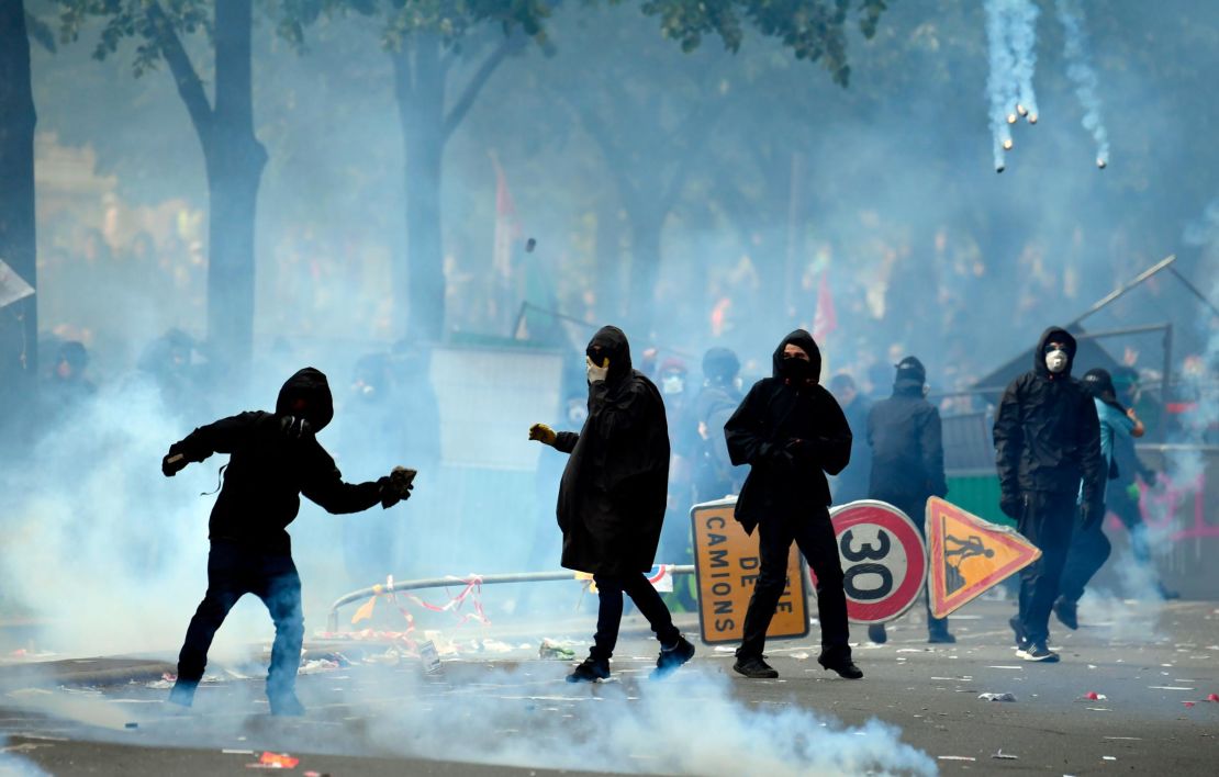 A protestor throws a stone towards police officials as teargas clouds rise during a demonstration on the sidelines of a march for the annual May Day rally in Paris.