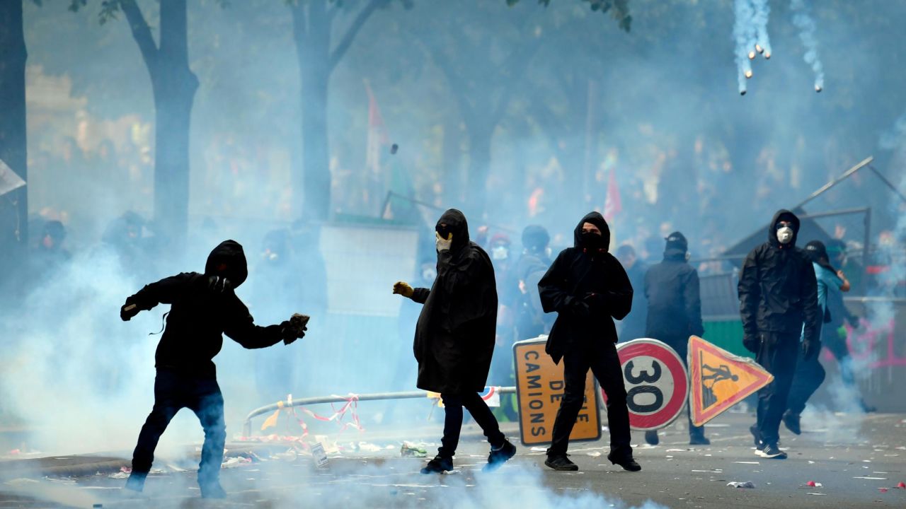 A protestor throws a stone towards police officials as teargas clouds rise during a demonstration on the sidelines of a march for the annual May Day rally in Paris.