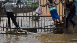 Pedestrian use a metal fence to cross, as they wade through the flooded road on their way to work following heavy rainfall, on March 15, 2018 in Nairobi.
