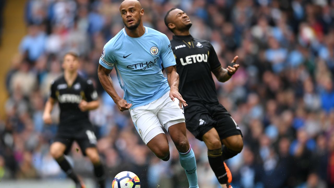MANCHESTER, ENGLAND - APRIL 22:  Vincent Kompany of Manchester City runs with the ball whilst Jordan Ayew of Swansea City reacts during the Premier League match between Manchester City and Swansea City at Etihad Stadium on April 22, 2018 in Manchester, England.  (Photo by Laurence Griffiths/Getty Images)