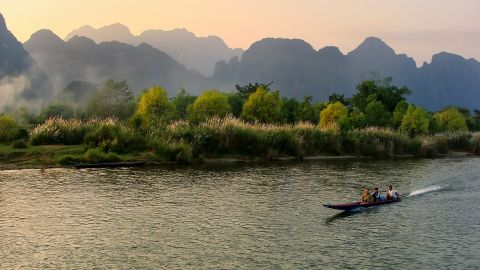 VANG VIENG, LAOS - NOVEMBER 25: Motorboat moving on Nam Song River at sunset on November 25, 2011 in Vang Vieng, Laos. Vang Vieng is a popular destination for tourism in a limestone karst landscape.