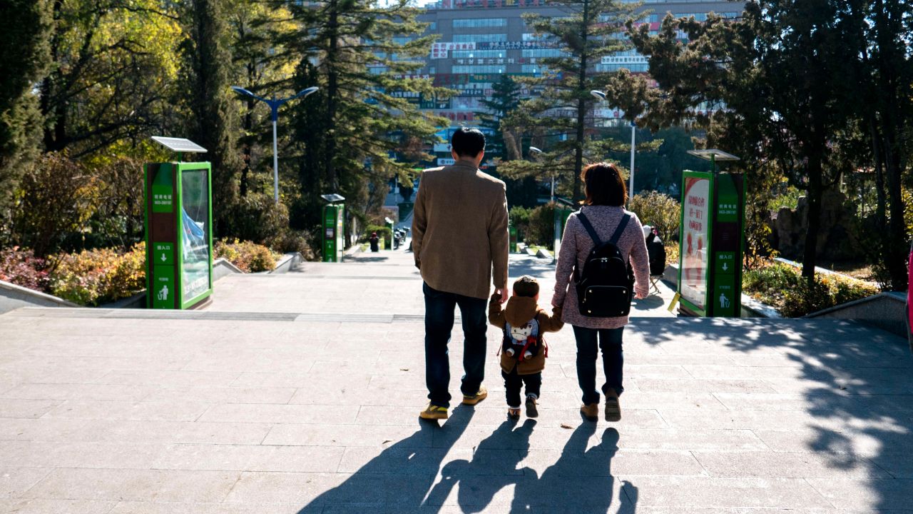Young parents take their only kid's hand walking on the road.