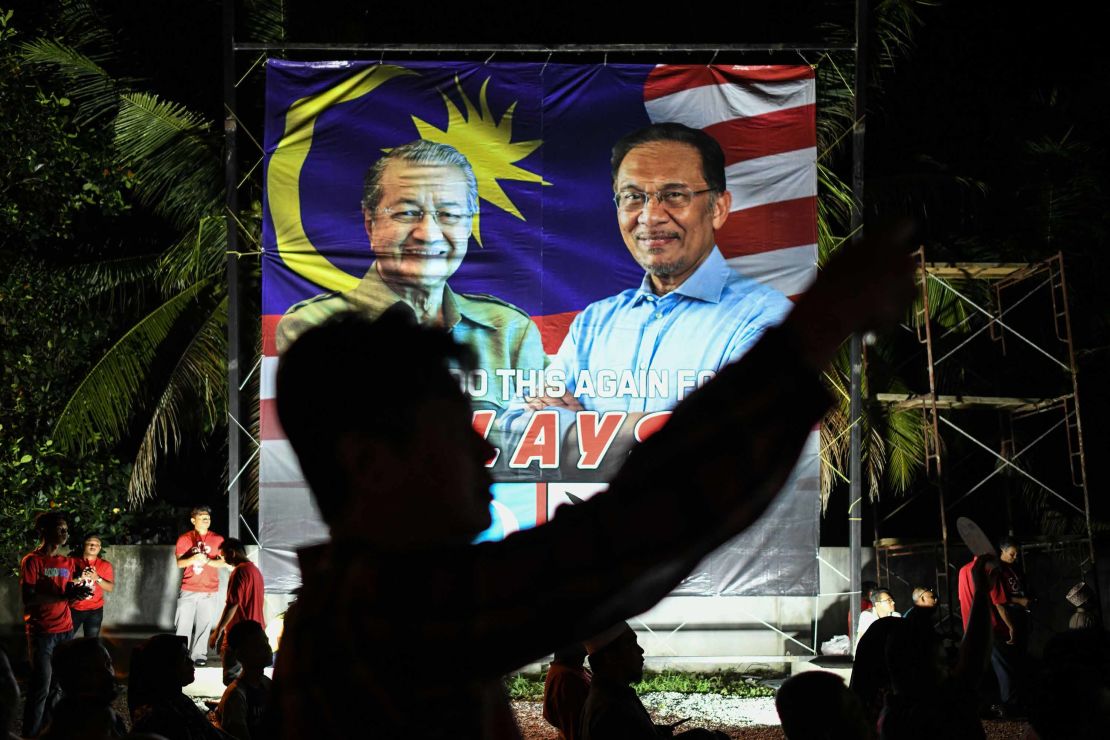 A supporter takes pictures in front of a banner showing former Malaysian Prime Minister Mahathir Mohamad  and Anwar Ibrahim during a rally before the election. 