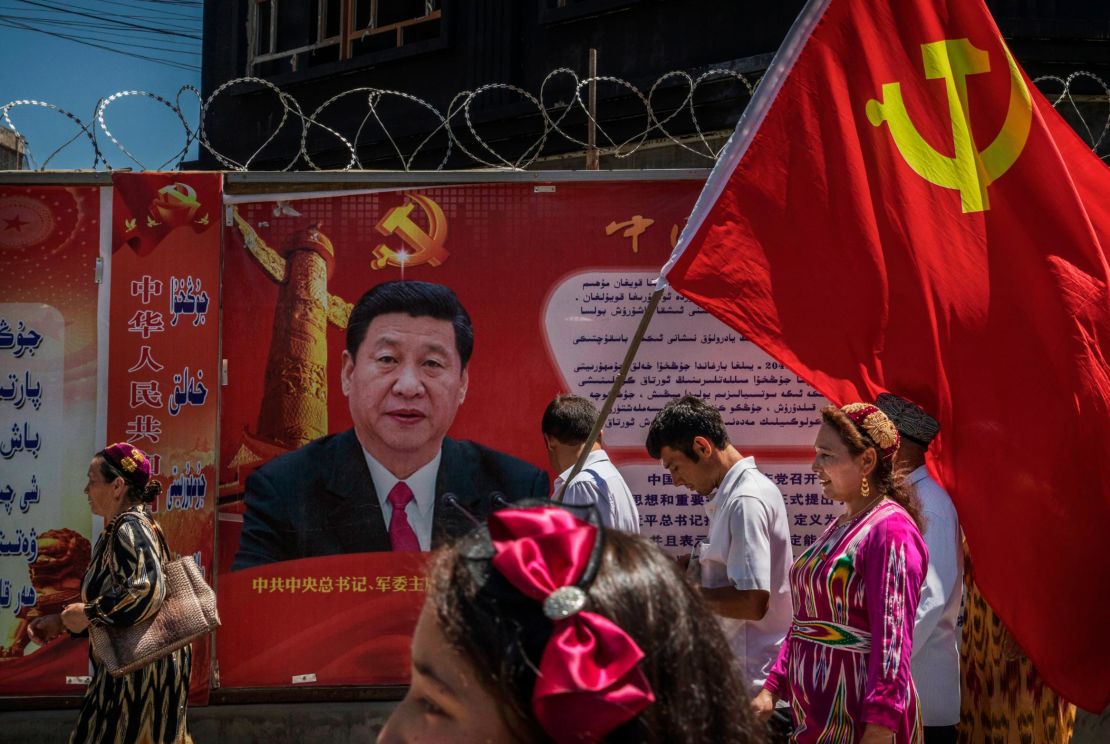 Ethnic Uyghur members of the Communist Party of China carry a flag past a billboard of Chinese President Xi Jinping as they take part in an organized tour on June 30, 2017 in the old town of Kashgar, Xinjiang.