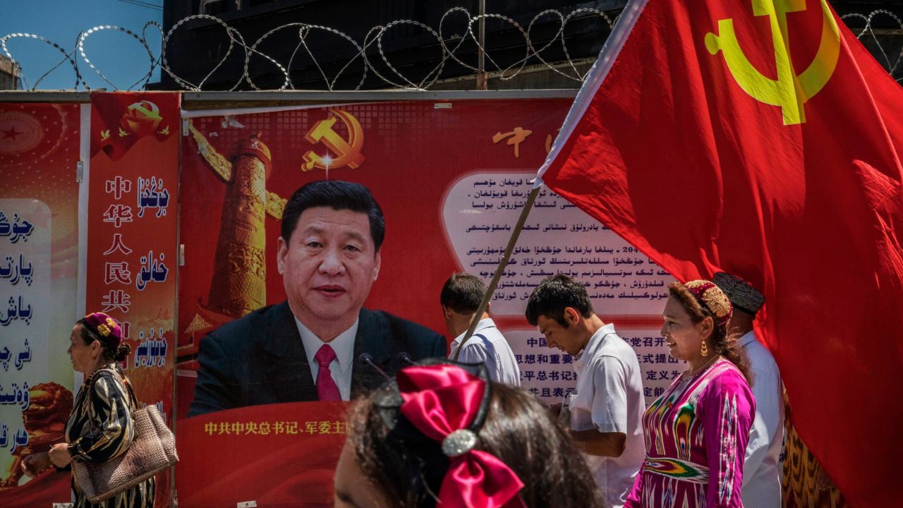 Ethnic Uyghur members of the Communist Party of China carry a flag past a billboard of Chinese President Xi Jinping as they take part in an organized tour on June 30, 2017 in the old town of Kashgar, Xinjiang.