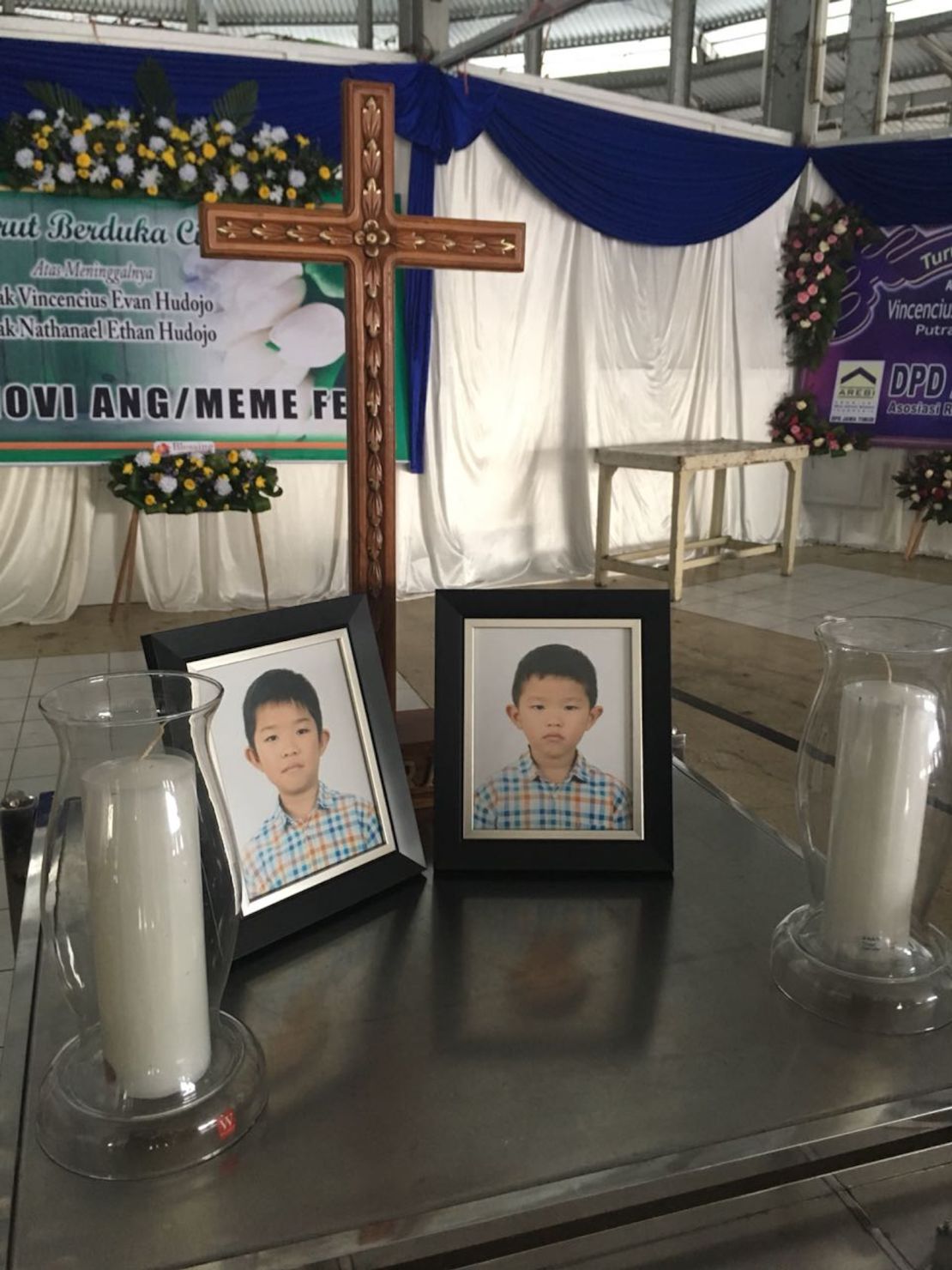 Photos of Vincensius Evan Hudojo and Nathanael Ethan Hudojo are displayed at a funeral home.