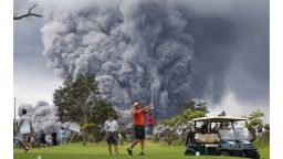  People play golf as an ash plume rises in the distance from the Kilauea volcano on Hawaii's Big Island on May 15, 2018 in Hawaii Volcanoes National Park, Hawaii. 