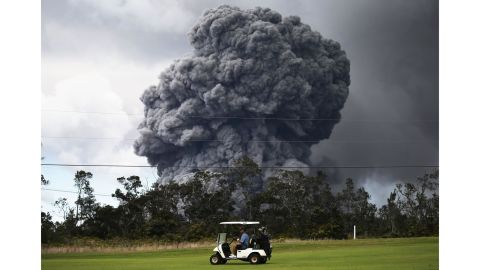 A man drives a golf cart at a golf course as an ash plume rises in the distance from the Kilauea volcano on Hawaii's Big Island 