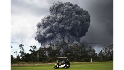 A man drives a golf cart at a golf course as an ash plume rises in the distance from the Kilauea volcano on Hawaii's Big Island