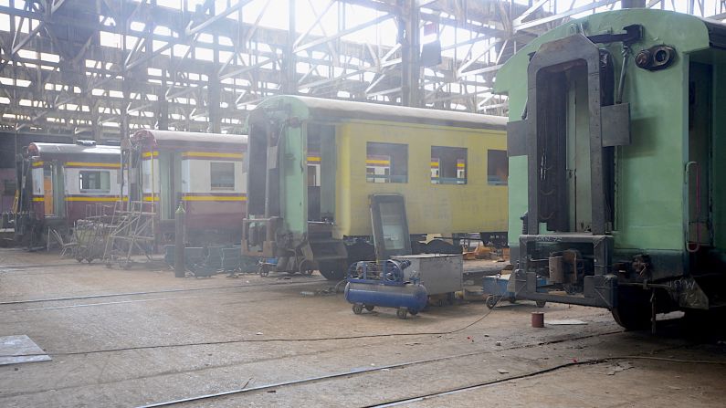 <strong>Makkasan repair yard:</strong> Sunlight and dust combine to shroud rail cars under repair inside a cavernous building, part of the 186-acre main repair yard for the State Railway of Thailand.  
