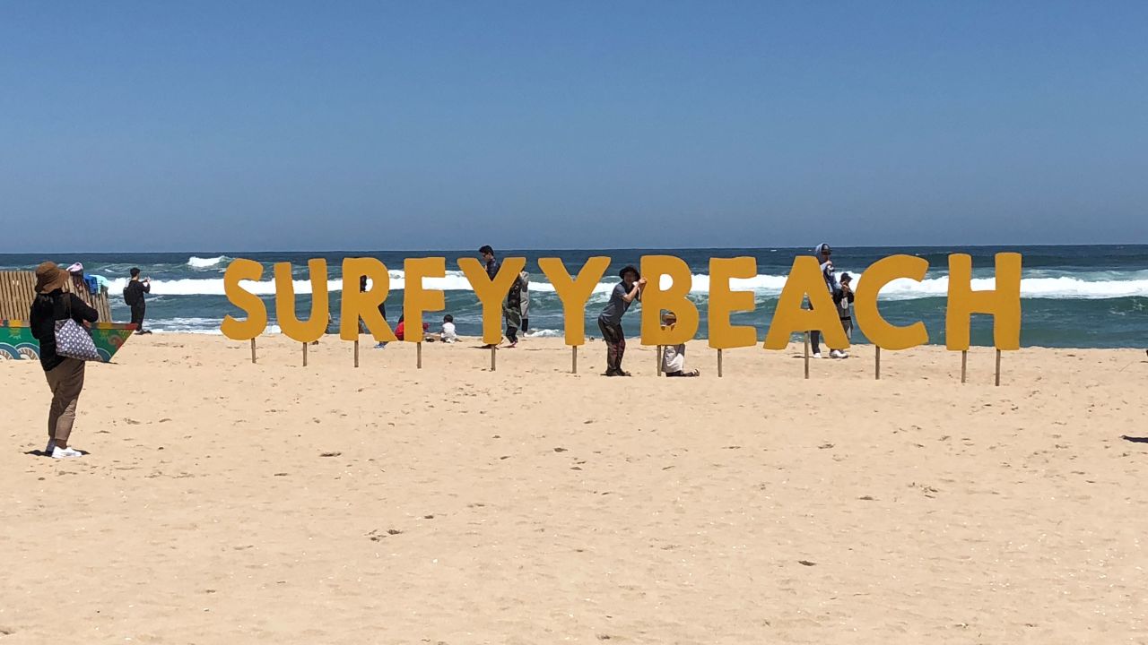 Tourists pose in front of a "Surfyy Beach" sign at Hajodae Beach on South Korea's east coast.