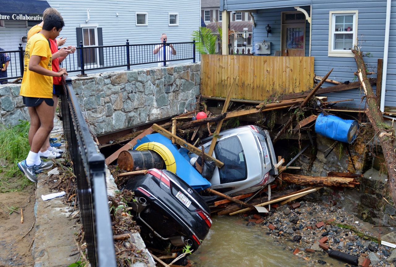 Residents gather by a bridge Monday to look at some cars that were left crumpled by the floods.