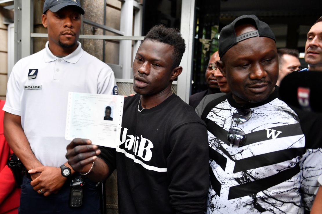Flanked by his older brother, Gassama holds his temporary residence permit after receiving it Tuesday.