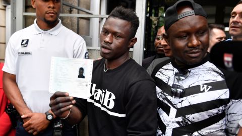 Flanked by his older brother, Gassama holds his temporary residence permit after receiving it Tuesday.
