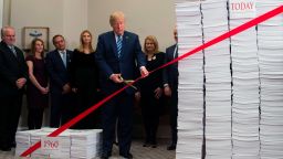 US President Donald Trump uses gold scissors to cut a red tape tied between two stacks of papers representing the government regulations of the 1960s (L) and the regulations of today (R) after he spoke about his administration's efforts in deregulation in the Roosevelt Room of the White House in Washington, DC on December 14, 2017. / AFP PHOTO / SAUL LOEB        (Photo credit should read SAUL LOEB/AFP/Getty Images)