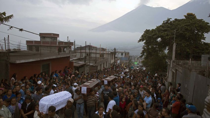 People carry the coffins of seven people who died during the eruption of the Volcan de Fuego, which in Spanish means Volcano of Fire, in the background, to the cemetery in San Juan Alotenango, Guatemala, Monday, June 4, 2018. Residents of villages skirting the volcano began mourning the dead after an eruption buried them in searing ash and mud. (AP Photo/Luis Soto)