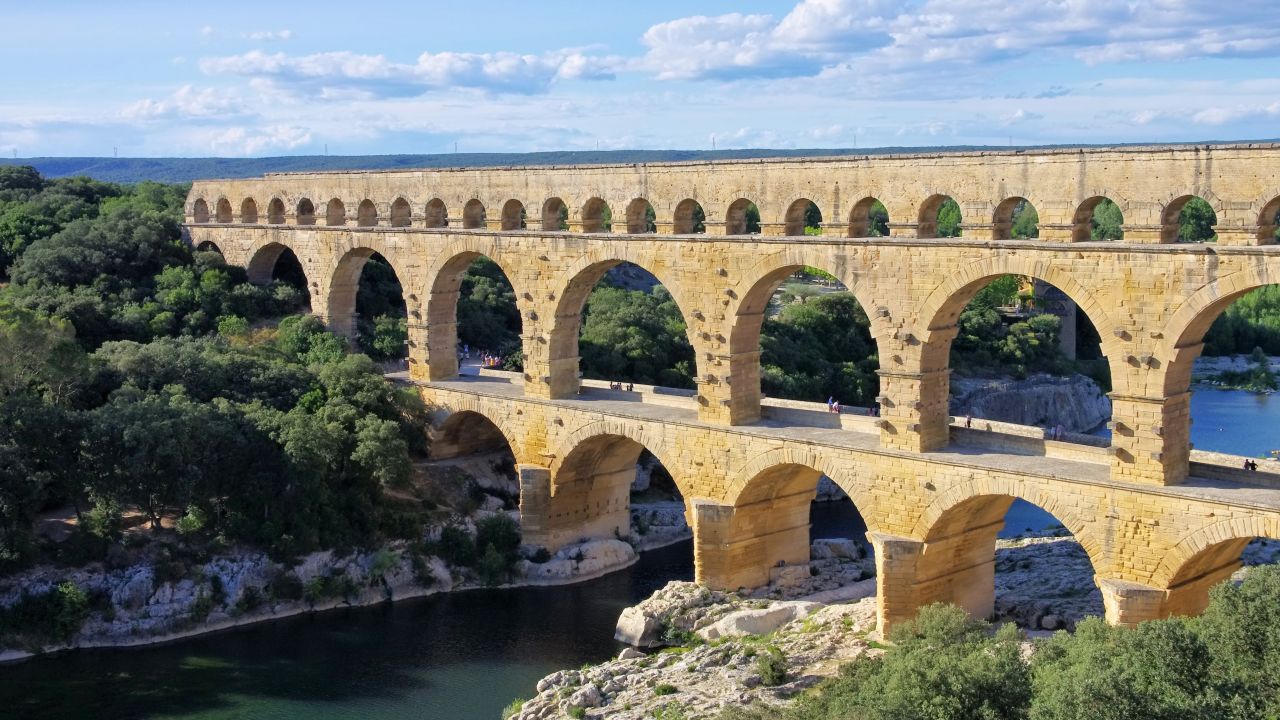 Le Pont Du Gard is an ancient Roman aqueduct bridge that crosses the Gard river in southern France. Built by the Romans in the 1st century AD, the bridge has three levels of arches and formerly carried an estimated 44 million gallons of water a day to the city of Nimes.