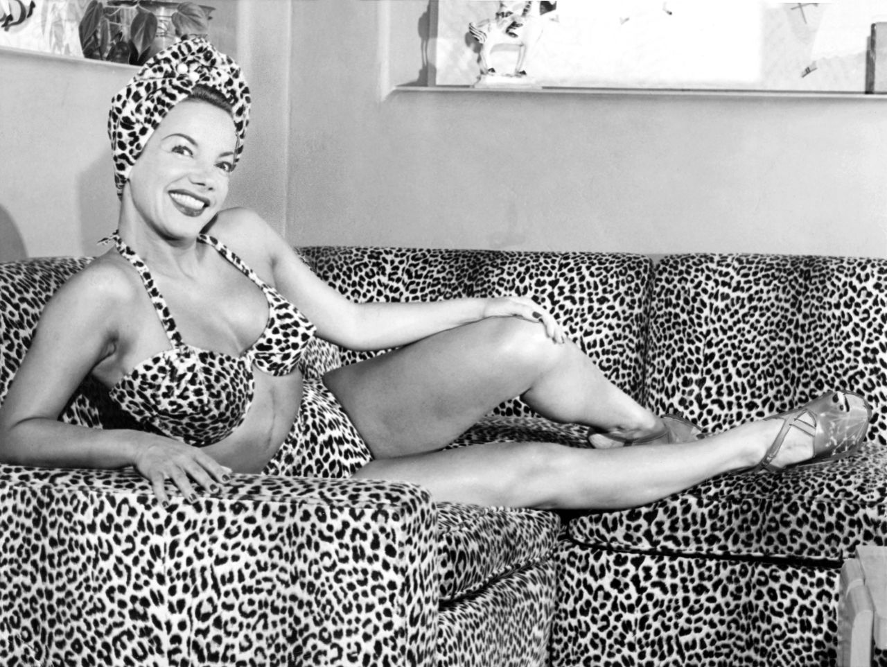 Carmen Miranda wears a leopard spotted bikini and head wrap on a leopard spotted couch in 1948.