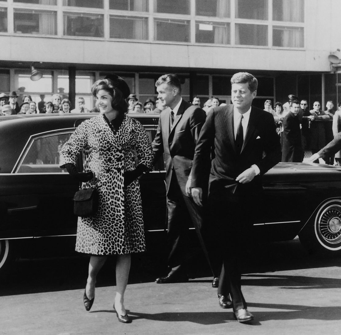 Escorted by President Kennedy, Jacqueline Kennedy departs for a trip to India and Pakistan wearing an Oleg Cassini leopard skin coat in 1962.