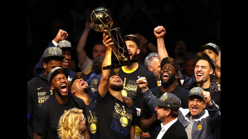 Stephen Curry, center, of the Golden State Warriors, celebrates with the Larry O'Brien Trophy after defeating the Cleveland Cavaliers during Game Four of the <a href="index.php?page=&url=http%3A%2F%2Fwww.cnn.com%2F2018%2F05%2F31%2Fsport%2Fgallery%2Fnba-finals-2018%2Findex.html" target="_blank">NBA Finals</a> on Friday, June 8, in Cleveland, Ohio. The Warriors defeated the Cavaliers 108-85. The Warriors have won back-to-back NBA titles and this is their third title in four years. 